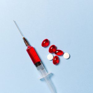 Syringe with red liquid and pills on a blue backdrop symbolizing medical treatment.
